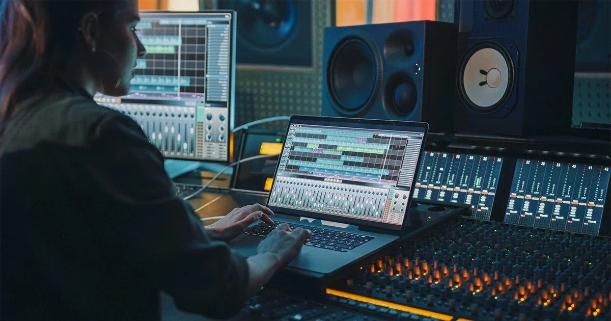 A woman focused on her laptop while in a recording studio environment